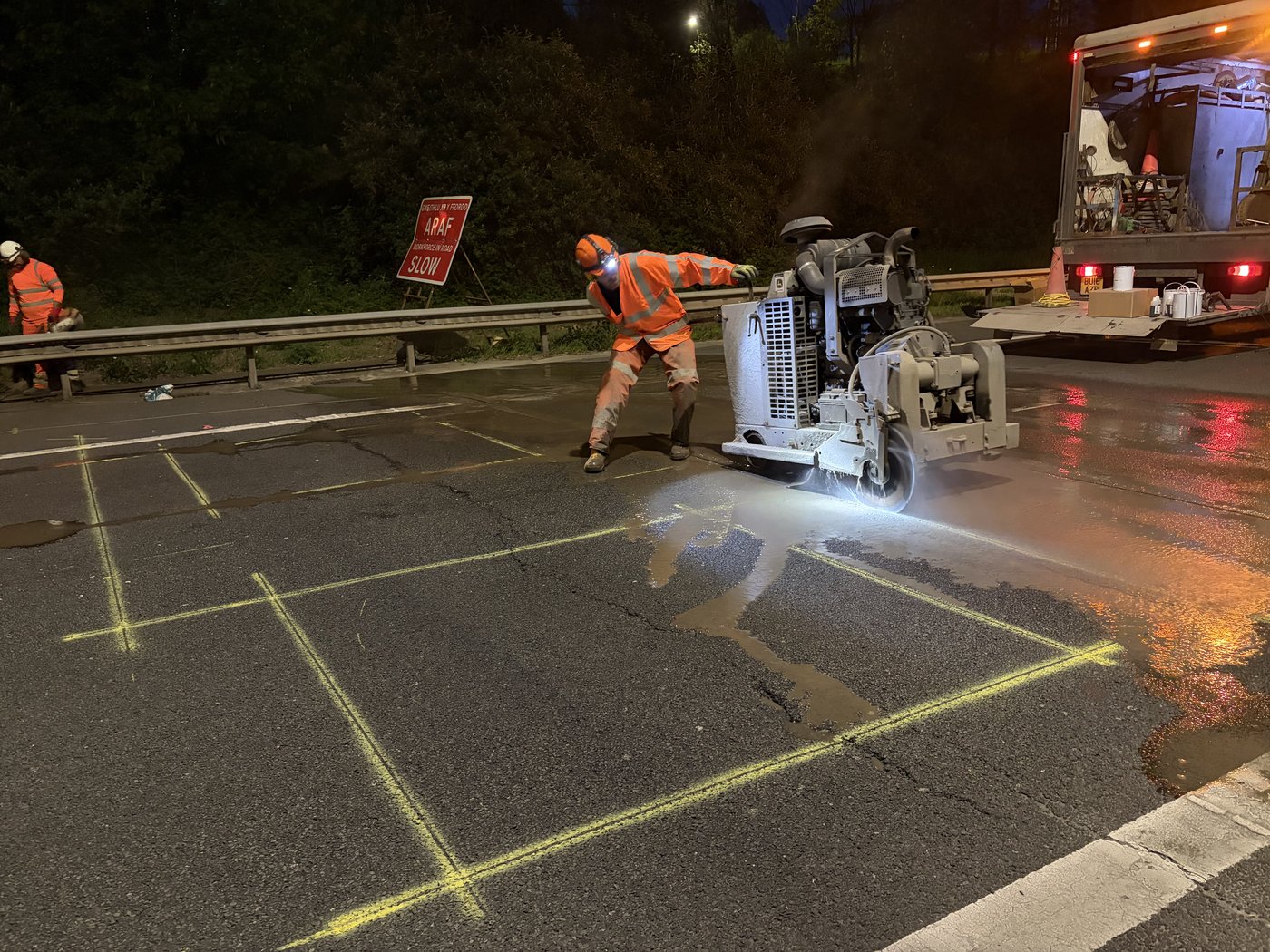 Field engineer cutting a loop slot into the road surface at night with a road saw